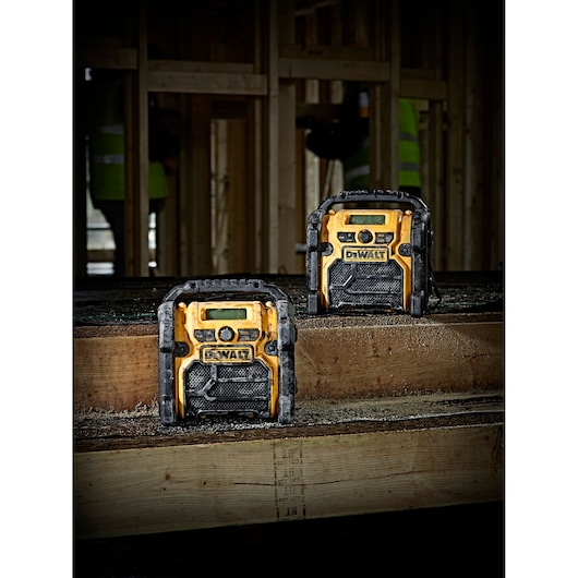 Two DEWALT DCR019 radios on a wooden workbench in a construction site with unfinished wood framing.
