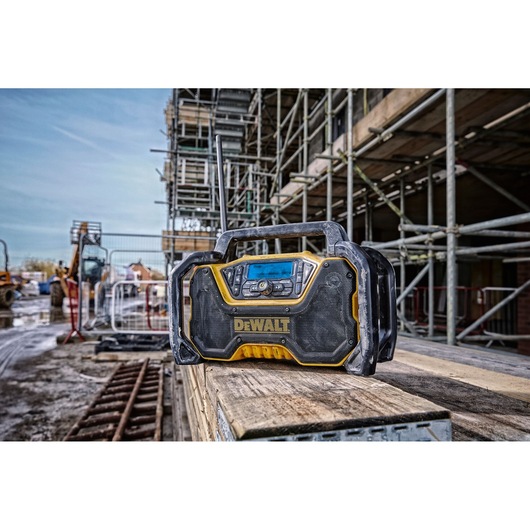 DEWALT portable radio sits on wooden planks at a construction site, surrounded by scaffolding and equipment.
