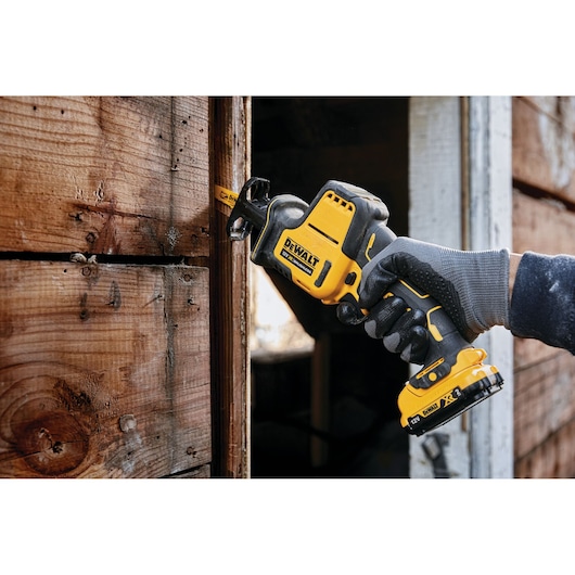 DEWALT cordless reciprocating saw cutting wood, held by gloved hand during outdoor carpentry work.