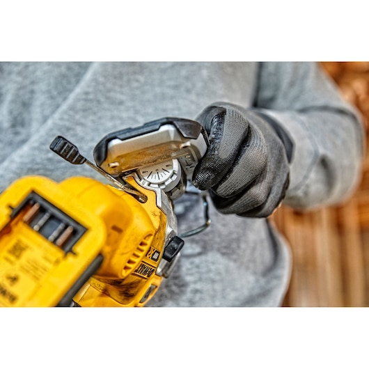 Gloved hand adjusts a yellow DEWALT jigsaw tool, focusing on the angle adjustment dial.