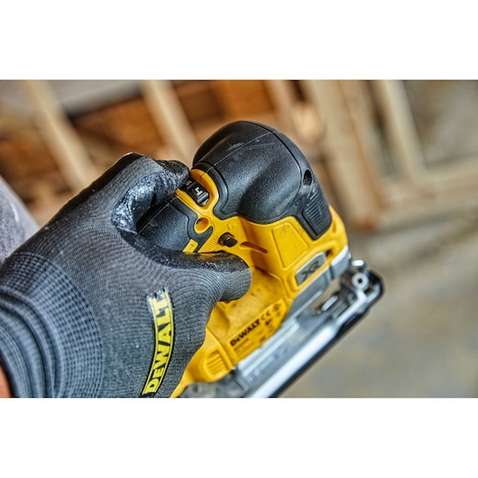 Gloved hand adjusts a yellow DEWALT jigsaw tool indoors with visible settings and brand name.
