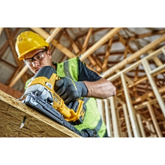 DEWALT cordless jigsaw cutting wood at a construction site, held by a worker in safety gear.