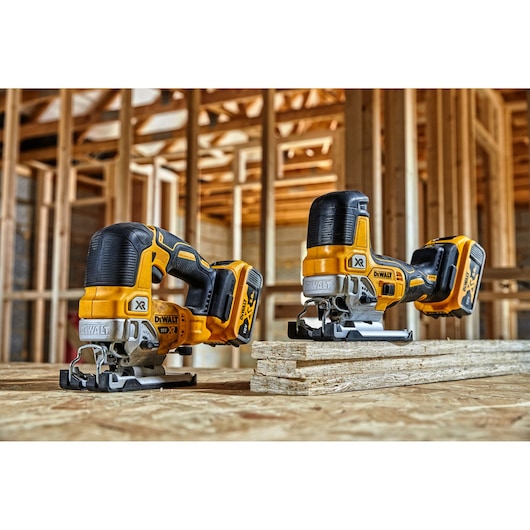 Two DEWALT cordless jigsaws on plywood sheets with wooden framing in the background at a construction site.