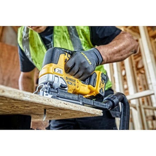 DEWALT cordless jigsaw cutting wood, operated by person wearing gloves and safety vest at construction site.