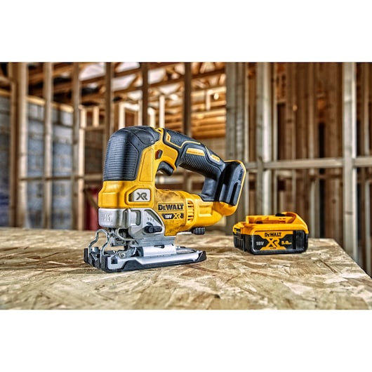 DEWALT cordless jigsaw and battery on wood surface in a construction area with exposed framing in the background.