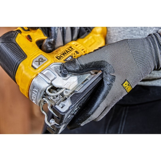 Gloved hand holding a yellow DEWALT XR 18V jigsaw power tool close-up.