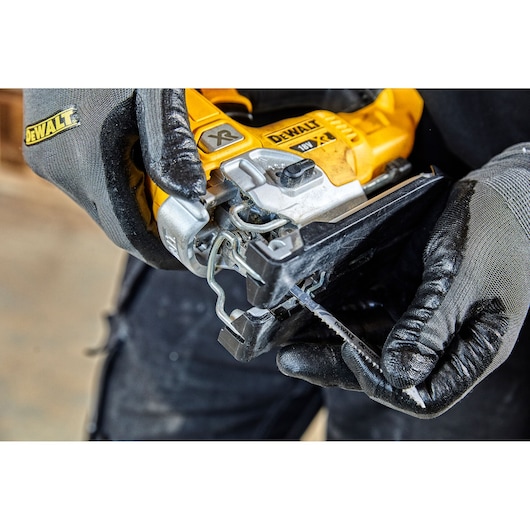 Gloved hands insert blade into yellow DEWALT DCS334 jigsaw tool during setup.