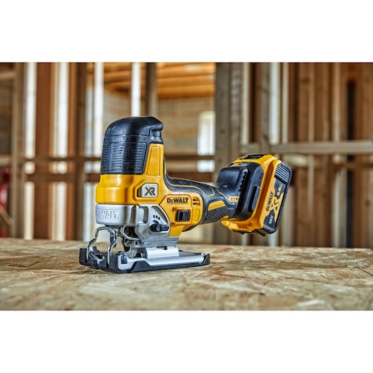 DEWALT cordless jigsaw, model DCS335P2, placed on a wooden surface at a construction site.