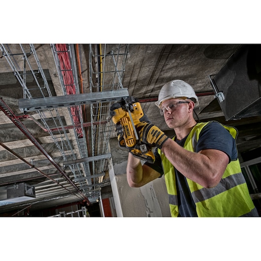 Worker using DEWALT DCS350NT tool to cut metal conduit on ceiling installation site.