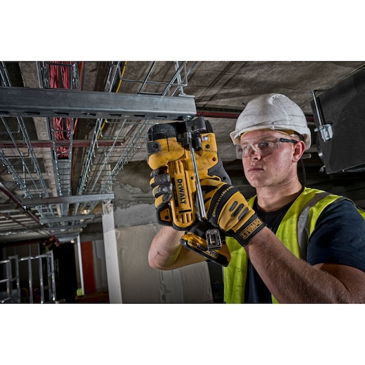 Worker using a DEWALT DCS350NT tool to cut metal conduit in an industrial setting, wearing gloves and safety gear.
