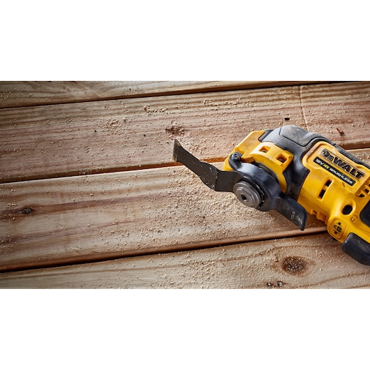 DEWALT cordless oscillating tool cutting wood, with sawdust on wooden planks.