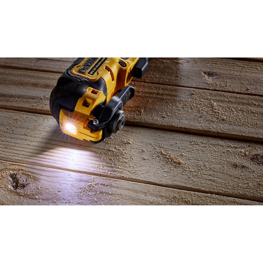 DEWALT cordless tool with LED light cutting wood, sawdust scattered on wooden surface.