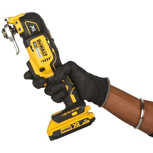 A gloved hand holding a DEWALT DCS355D2 cordless oscillating multi-tool with an 18V XR battery, isolated on a white background.