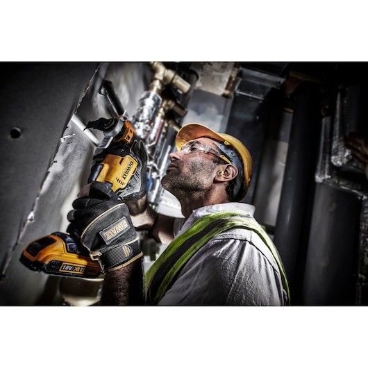 Worker uses a DEWALT DCS356NT cordless tool on a construction site, wearing gloves and a safety helmet.