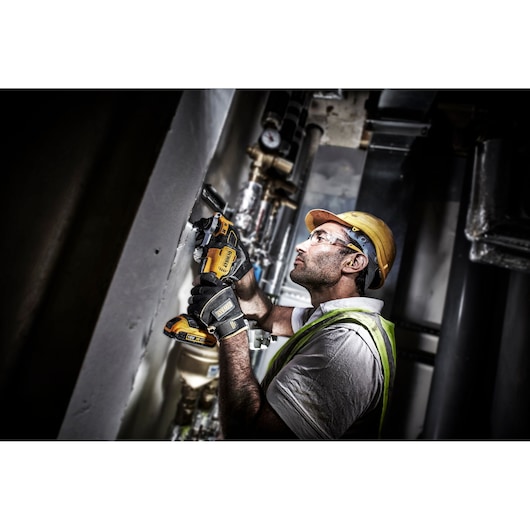 Worker uses DEWALT DCS356NT cordless tool on wall in industrial setting, wearing safety gear and gloves.