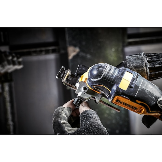 Gloved hand adjusts a DEWALT cordless oscillating multi-tool in an industrial workshop setting.