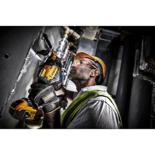 Worker uses DEWALT DCS356P2 cordless tool to cut material on a construction site, wearing safety gear.