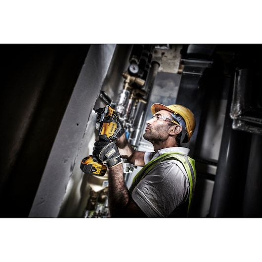 Worker using a DEWALT DCS356P2 cordless multi-tool to cut wall material inside an industrial setting.