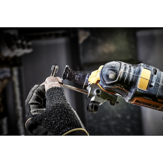 Gloved hand uses a DEWALT oscillating tool to cut metal in a workshop.