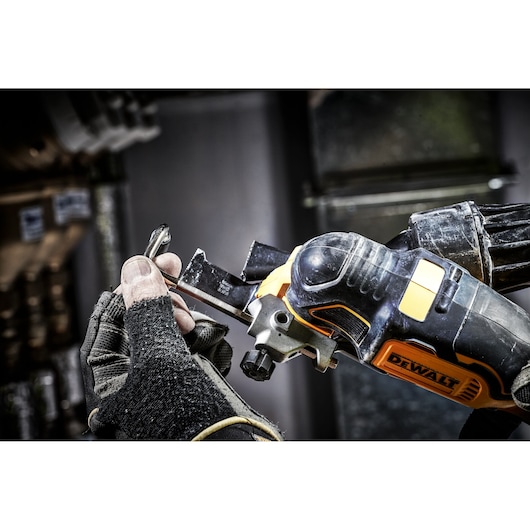 A gloved hand adjusts a DEWALT oscillating multi-tool using a wrench in a workshop setting.