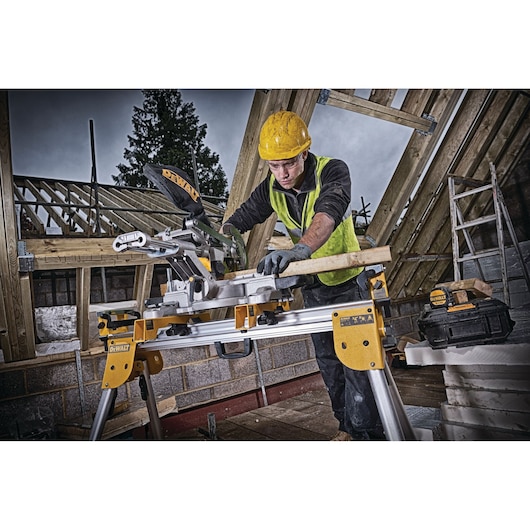 Worker uses DEWALT DCS365N saw to cut wood on a construction site with timber framing, safety gear worn.