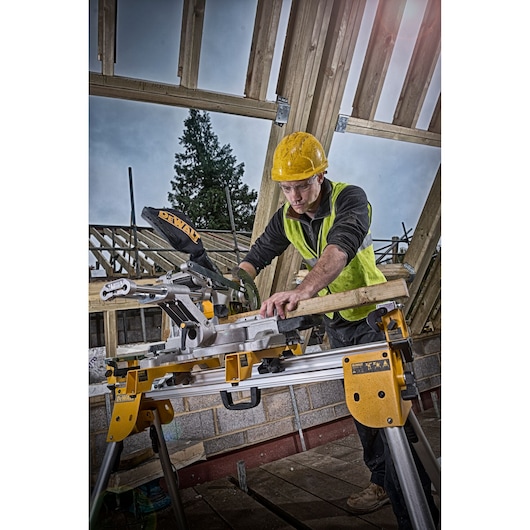 Worker uses DEWALT DCS365N saw to cut wood at a construction site with unfinished timber framing.