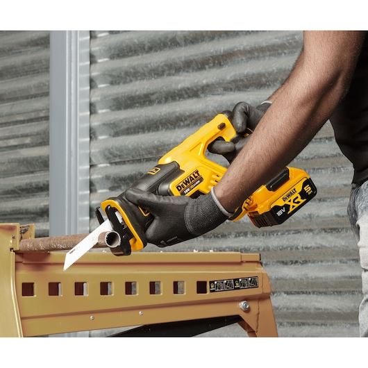 Person using a DEWALT cordless reciprocating saw to cut a metal pipe while wearing gloves.