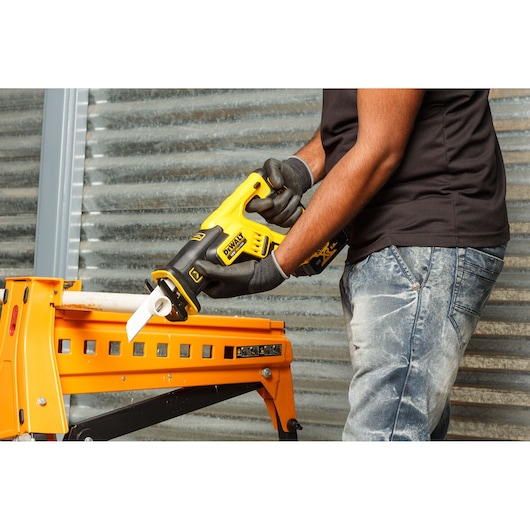Person using DEWALT DCS367P2 saw to cut a pipe held on a yellow workbench indoors.
