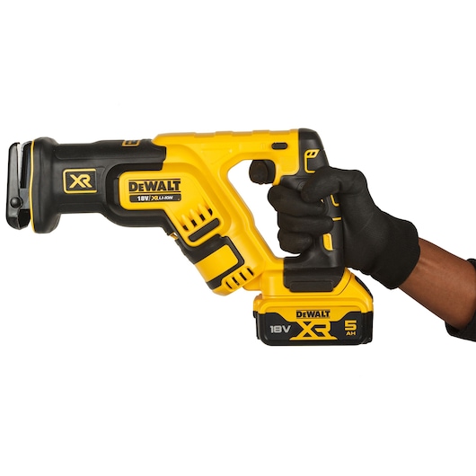 A hand wearing a black glove is holding a yellow and black DEWALT 18V XR lithium-ion cordless reciprocating saw with a 5Ah battery against a white background.