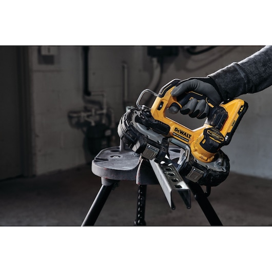 DEWALT cordless bandsaw cutting a metal piece, operated by a gloved hand in a workshop.