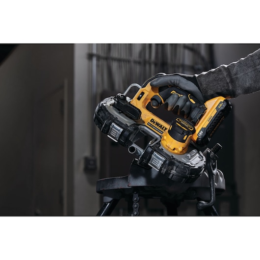 A DEWALT handheld bandsaw cutting metal tubing in an industrial setting. Gloved hand holds the tool.