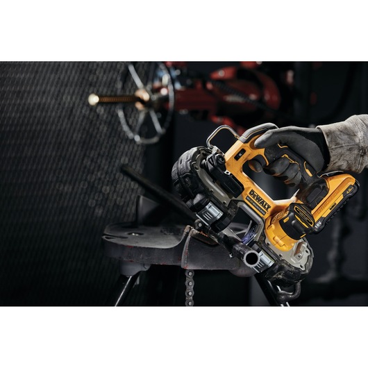 Gloved hand using Dewalt cordless band saw to cut metal pipe in a workshop setting.