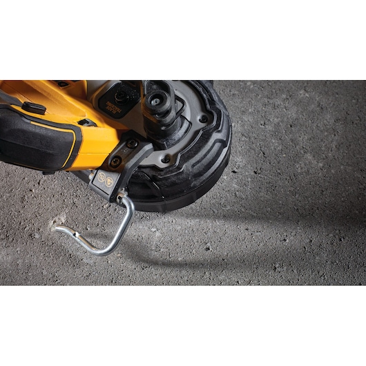 Close-up of a DEWALT portable power tool resting on a concrete surface, showing its hook and grip.