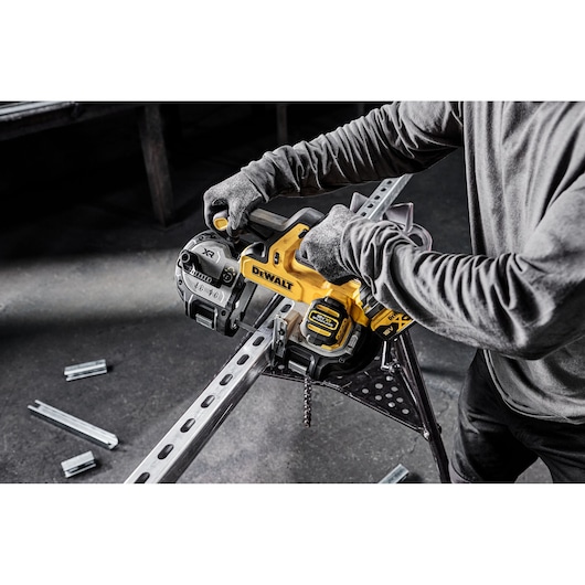 Person uses DEWALT cordless band saw to cut metal beam indoors. Saw and safety gloves are visible.