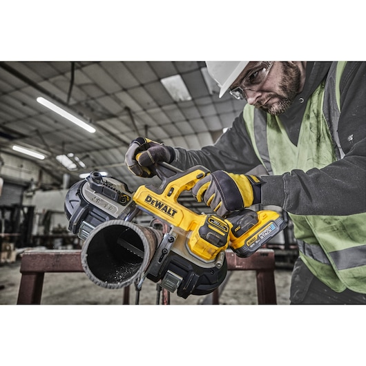 DEWALT cordless band saw cutting a metal pipe in an industrial workshop setting with gloved operator.