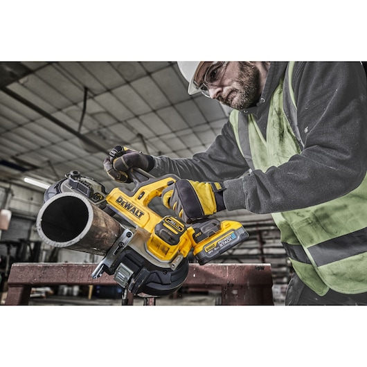 Worker uses DEWALT DCS378N cordless band saw to cut a metal pipe in an industrial setting.