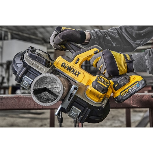 DEWALT cordless band saw cutting a metal pipe, held by gloved hands in an industrial workshop setting.