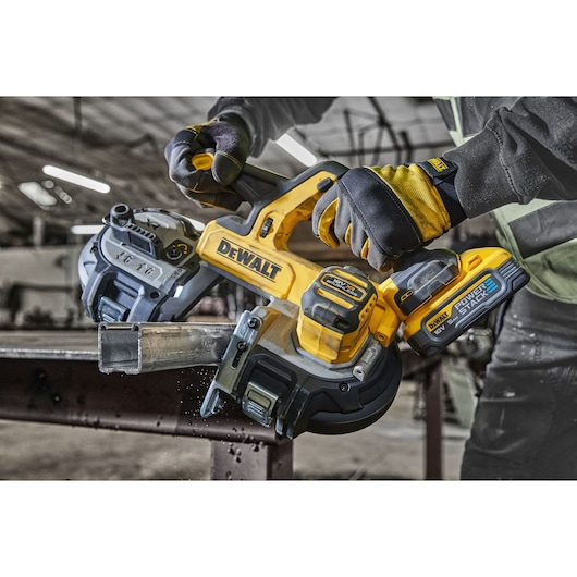 Worker uses a DEWALT cordless band saw to cut metal pipe in an industrial setting.
