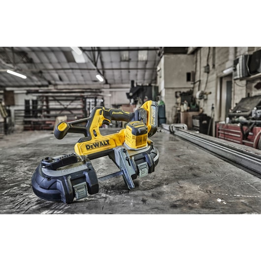 DEWALT cordless bandsaw placed on a workshop table with tools and equipment visible in the background.