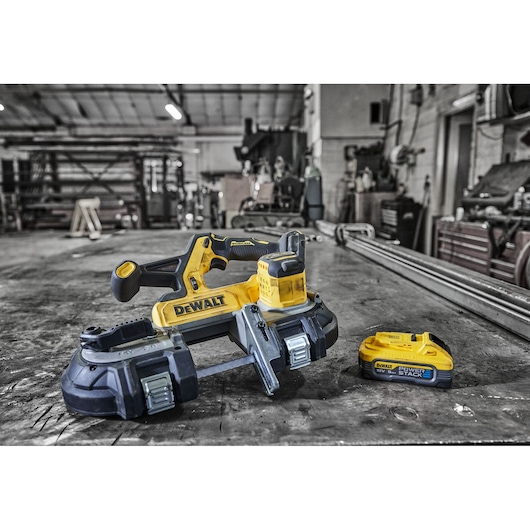 DEWALT cordless bandsaw and battery on a workshop table with industrial equipment in the background.