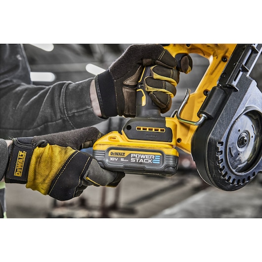 Gloved hands holding a DEWALT cordless circular saw with Power Stack battery in a workshop setting.