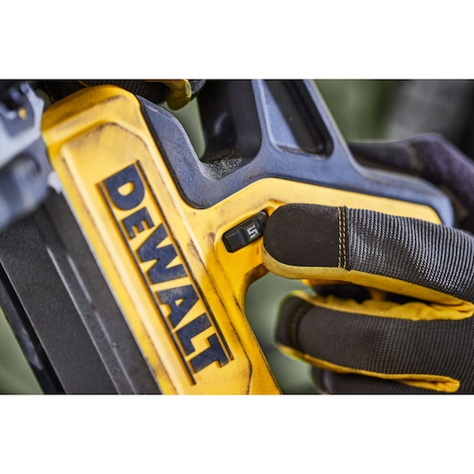 Gloved hand adjusting a switch on a yellow DEWALT tool, close-up view of branded equipment.