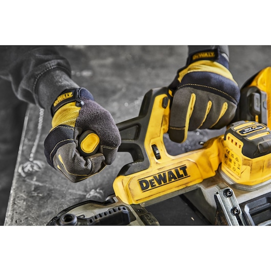 Gloved hands operate a yellow DEWALT power tool on a workshop table. Battery and brand logo are visible.