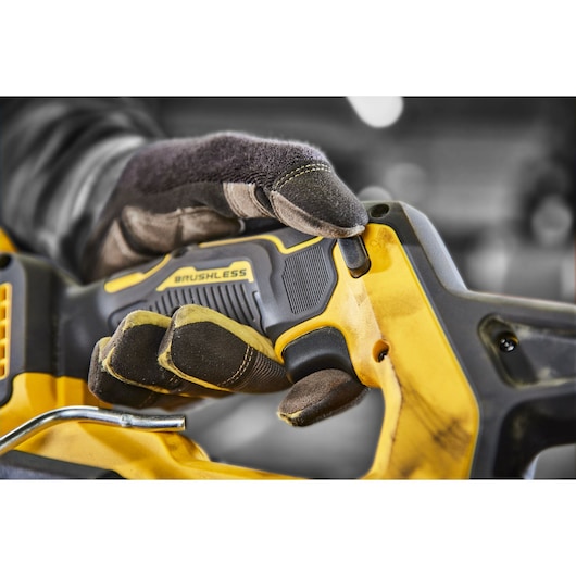 Gloved hand holding a yellow DEWALT brushless power tool, close-up of grip and control button.