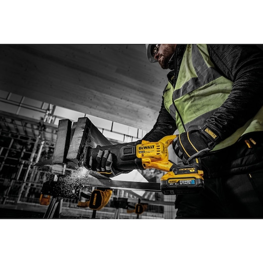 A person wearing safety gear uses a DEWALT cordless reciprocating saw, model DCS386H2T, with POWERSTACK technology to cut through a metal beam in a construction setting.