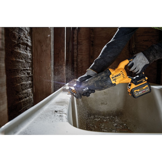 Person uses DEWALT cordless reciprocating saw to cut material near a bathtub during renovation.