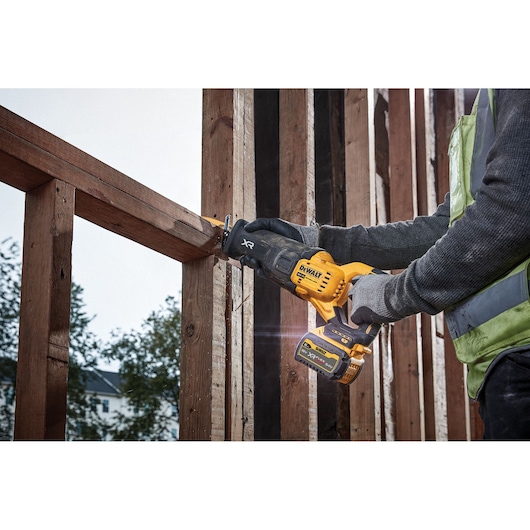 Person uses a DEWALT DCS386NT reciprocating saw to cut a wooden beam at a construction site.