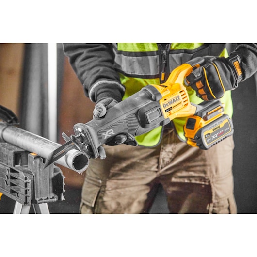 DEWALT cordless reciprocating saw cutting a metal pipe, held by a worker wearing gloves and safety vest.
