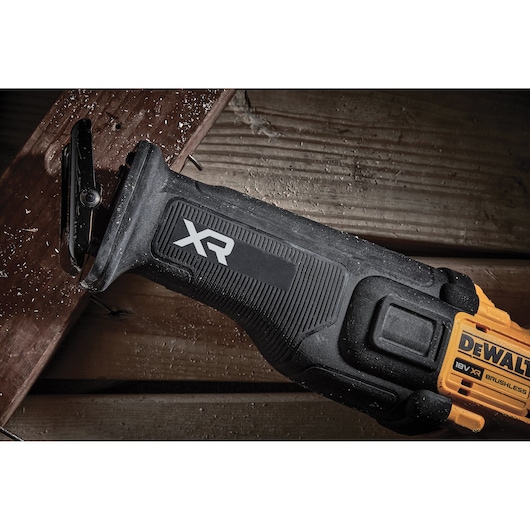 DEWALT XR cordless reciprocating saw cutting wood, close-up of tool and wood shavings.