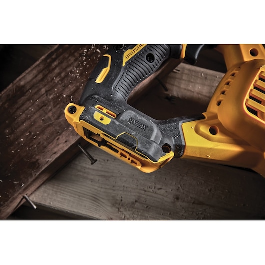 Close-up of DEWALT DCS386NT power tool handle on a wooden surface with nails and sawdust.